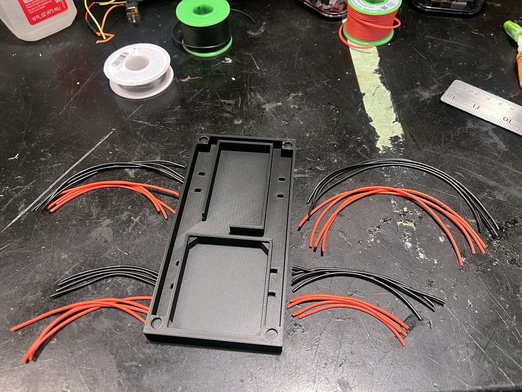 A 3D-printed chassis base surrounded by cut red and black motor leads