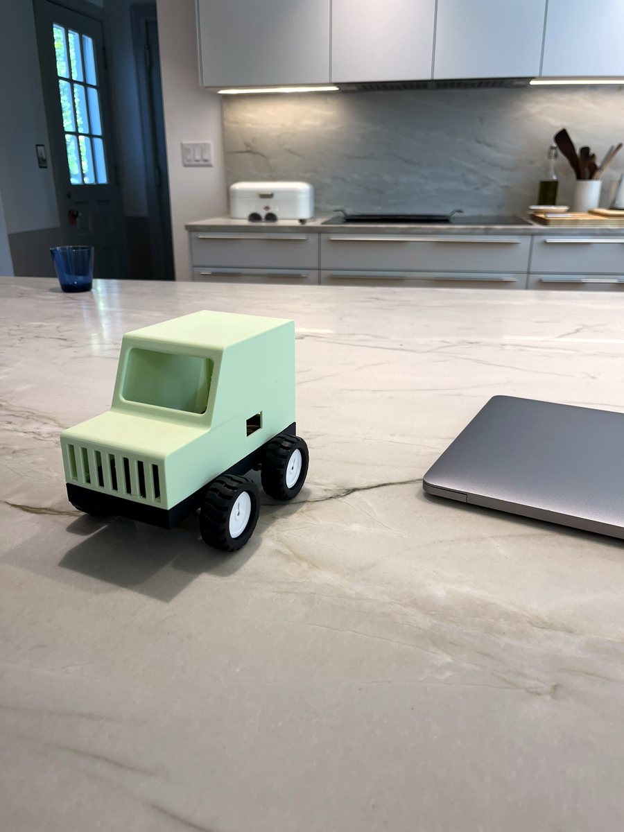 A mint green car on a kitchen counter next to a laptop
