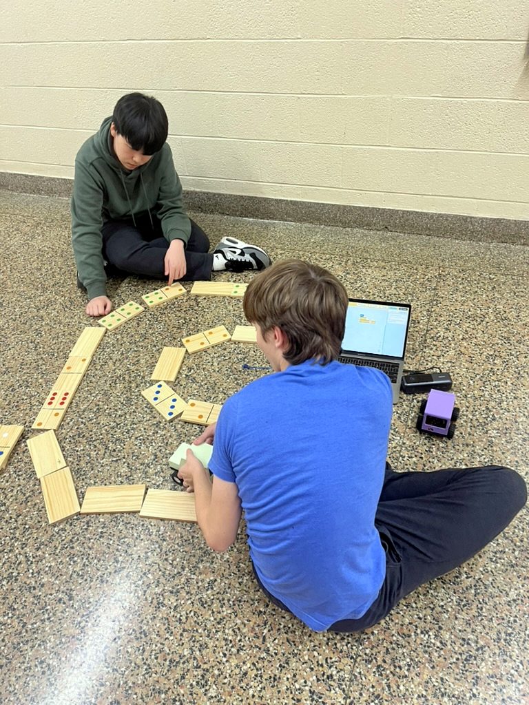 Two students programming a car beside a ring of giant dominoes